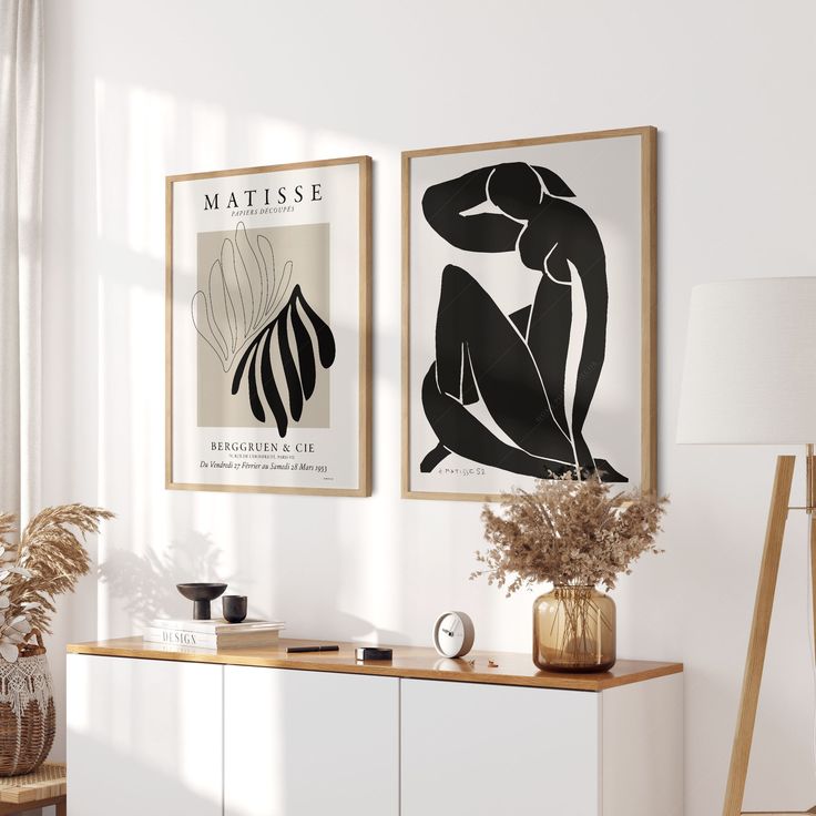 two framed art pieces hang on the wall next to a white sideboard and lamp