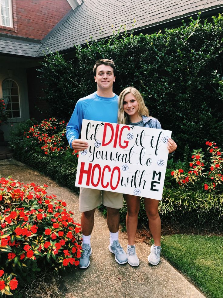 two people standing in front of a house holding a sign