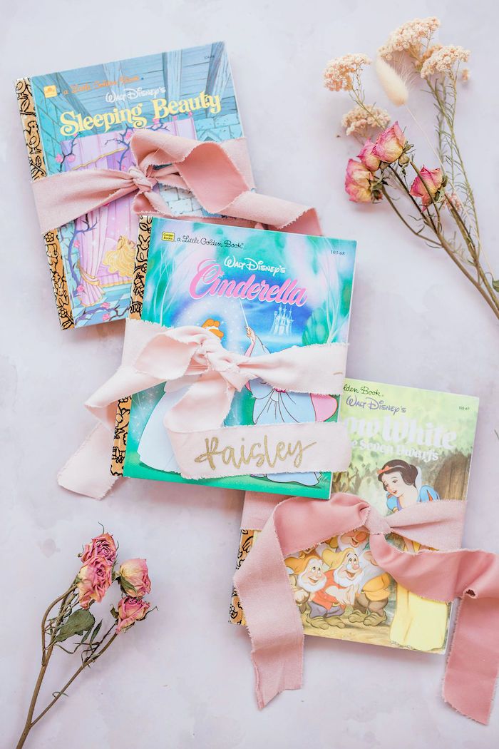 some books and flowers are laying on the table together with pink ribbon tied around them