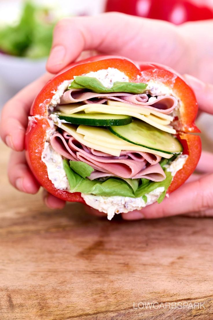 a person holding a sandwich with meat and veggies in it on a cutting board