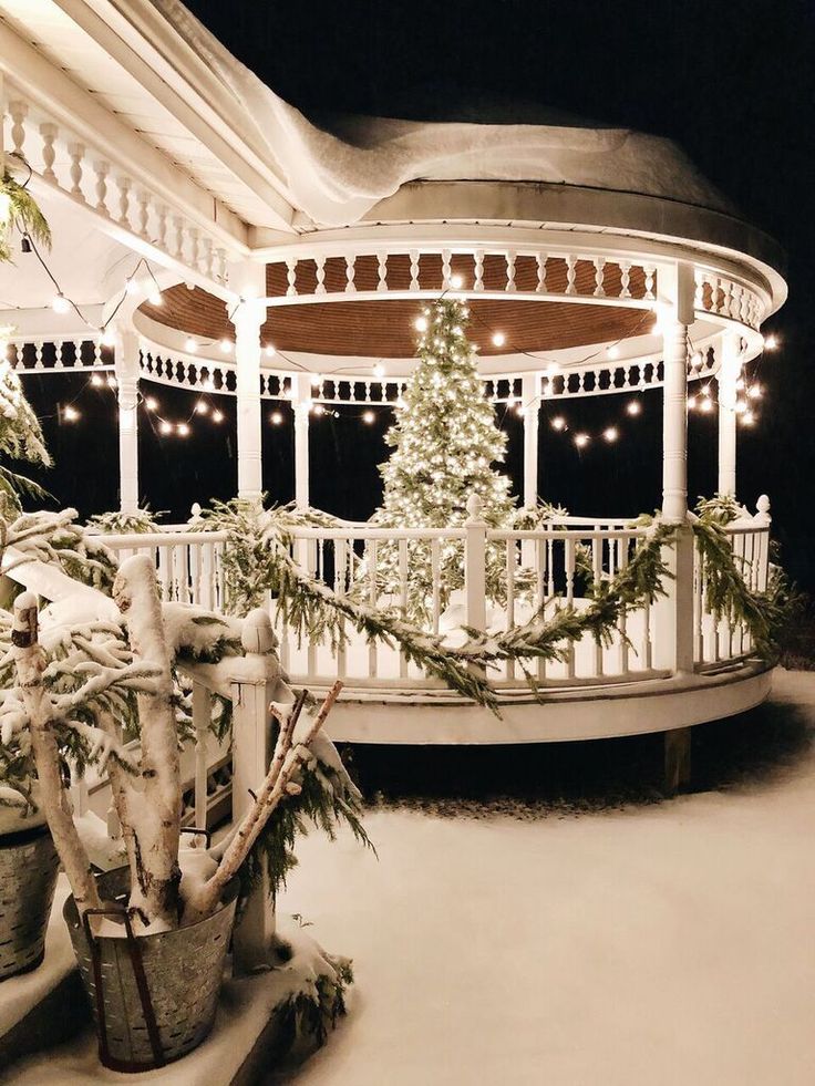 a white gazebo with christmas trees and lights on the porch in front of it