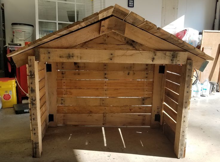 a small wooden dog house made out of pallet wood in a garage with no roof