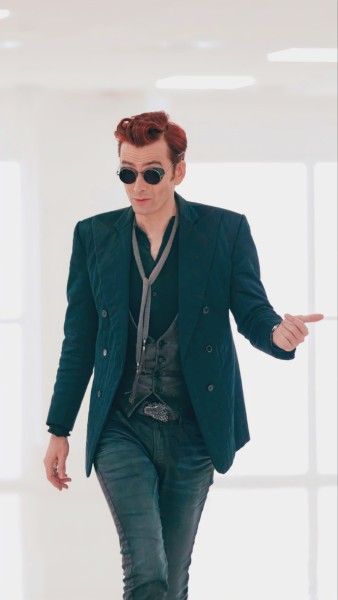 a man with red hair and sunglasses walks down the runway in a green blazer