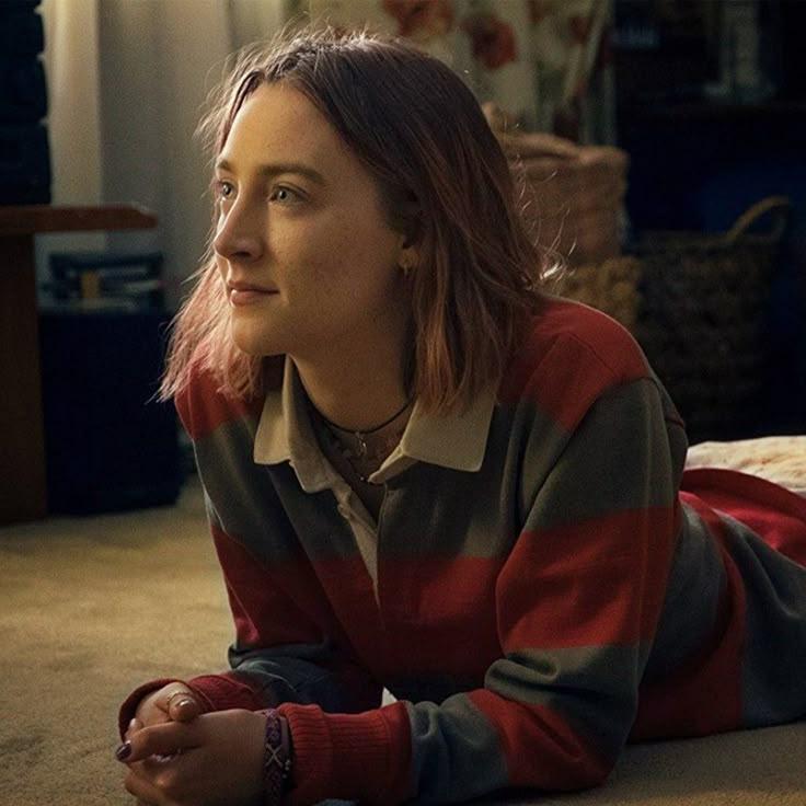 a young woman laying on the floor with a remote in her hand and looking off into the distance