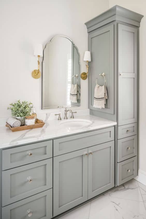 a white bathroom with gray cabinets and marble counter tops, along with a large mirror on the wall