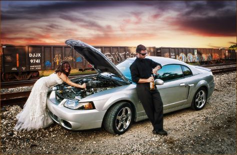 a man and woman standing next to a silver car with the hood open on it