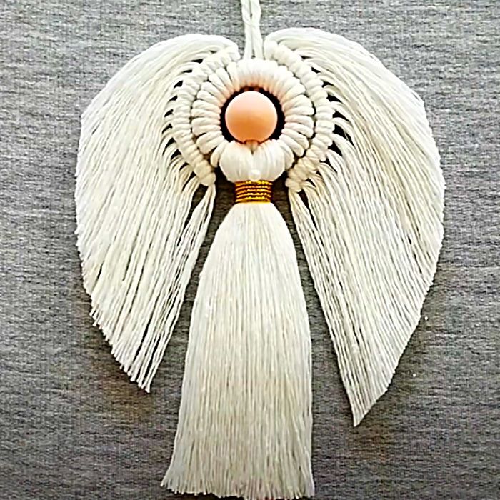 an angel ornament with white tassels and gold accents on a gray surface