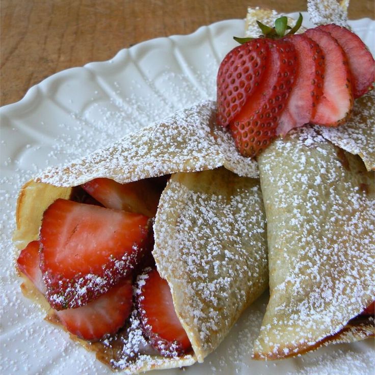 some strawberries and powdered sugar on top of pastries in a white plate