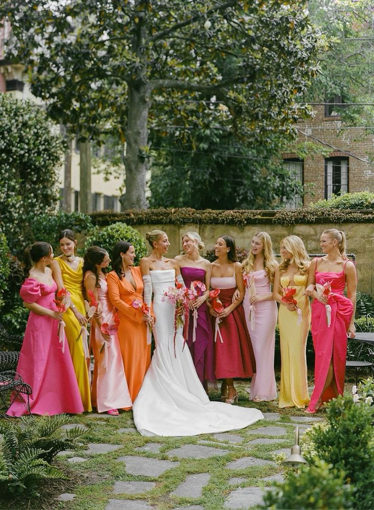 a group of women in dresses standing next to each other on a stone walkway near trees