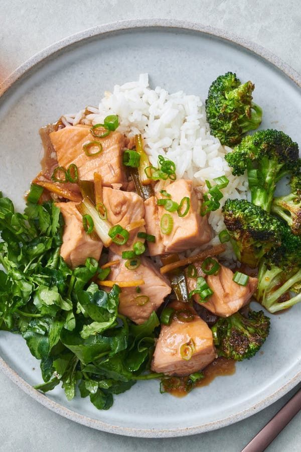 a white plate topped with meat and broccoli covered in sauce next to rice