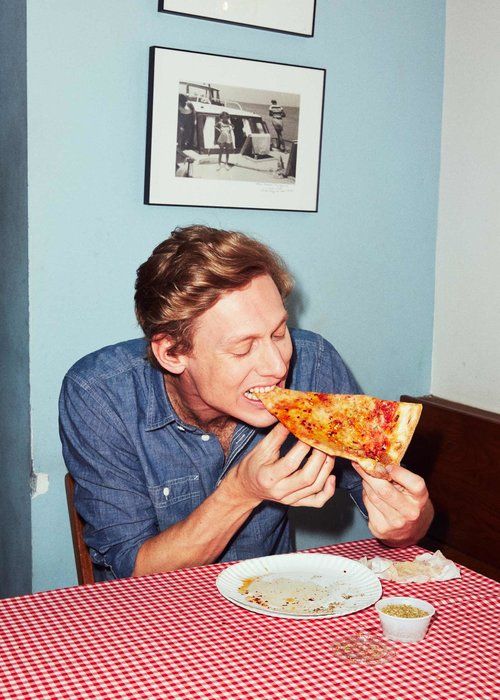 a man sitting at a table eating a slice of pizza