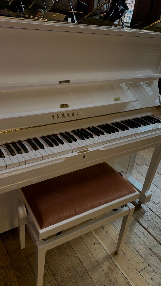 a white piano sitting on top of a hard wood floor next to a bench with a brown seat