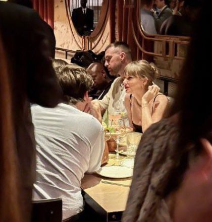 a group of people sitting at a table in a restaurant eating food and drinking wine