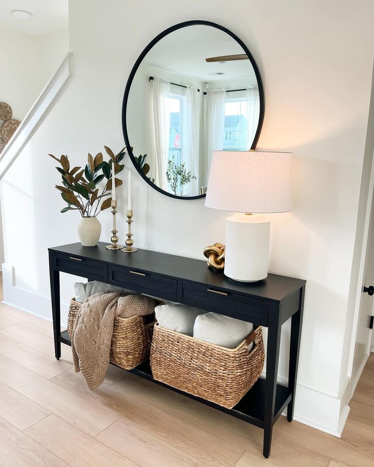 a black console table with baskets under it and a round mirror on the wall above