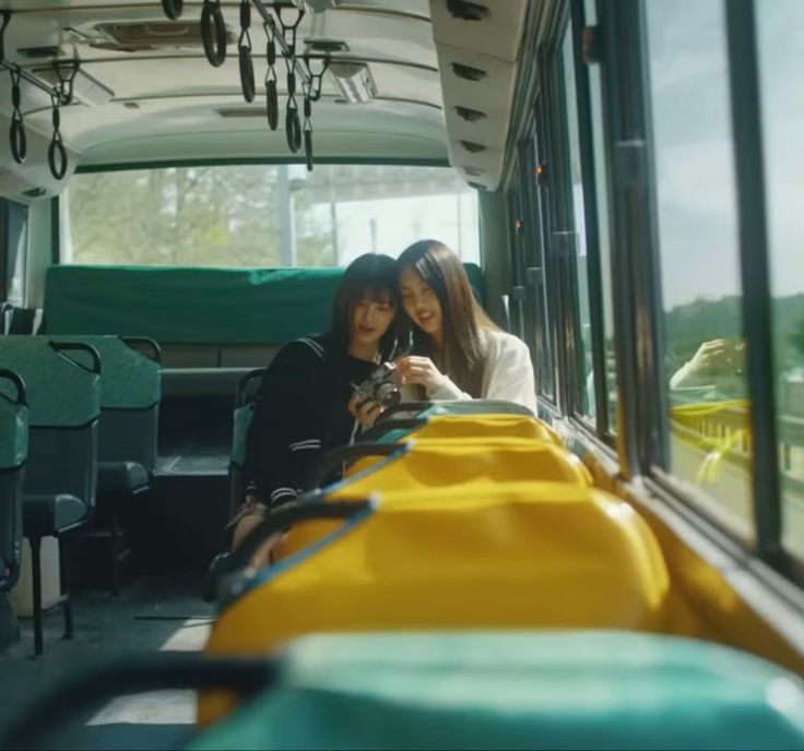 two young women sitting on the back of a bus looking at their cell phones in front of them