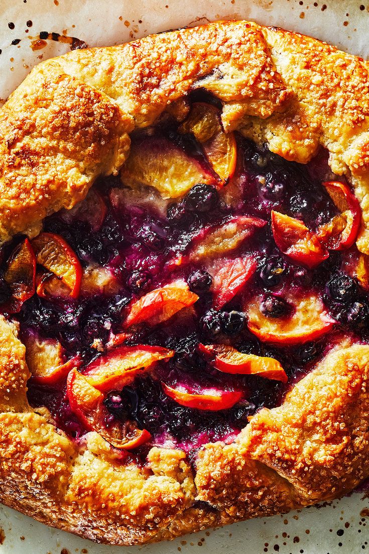 a pie with blueberries and peaches on it sitting on top of a piece of parchment paper