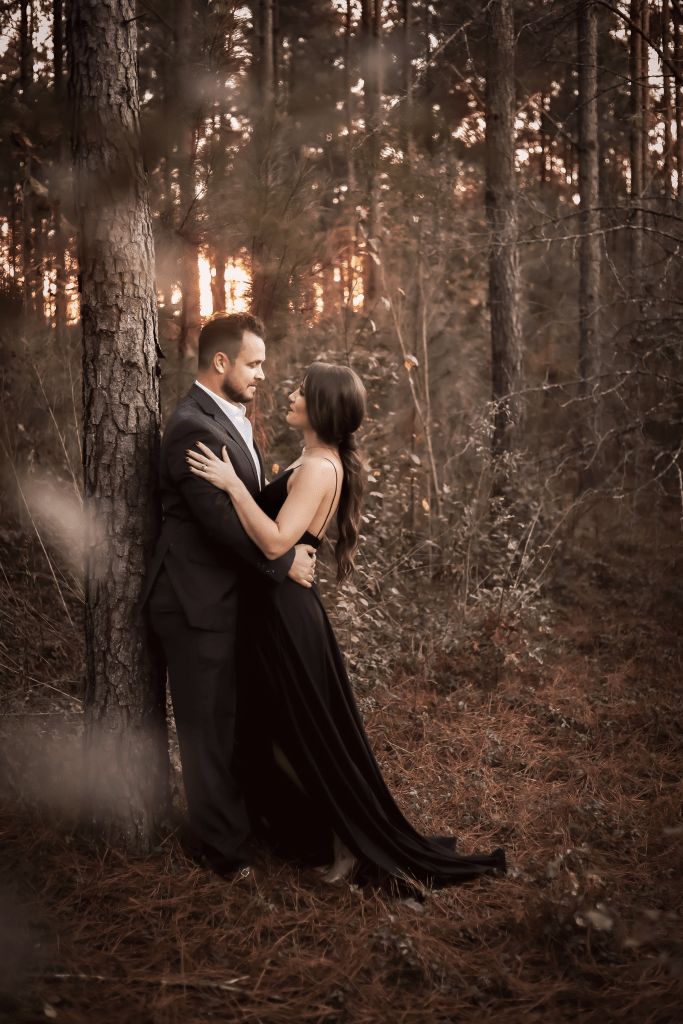 a man and woman standing next to each other near a tree in the middle of a forest