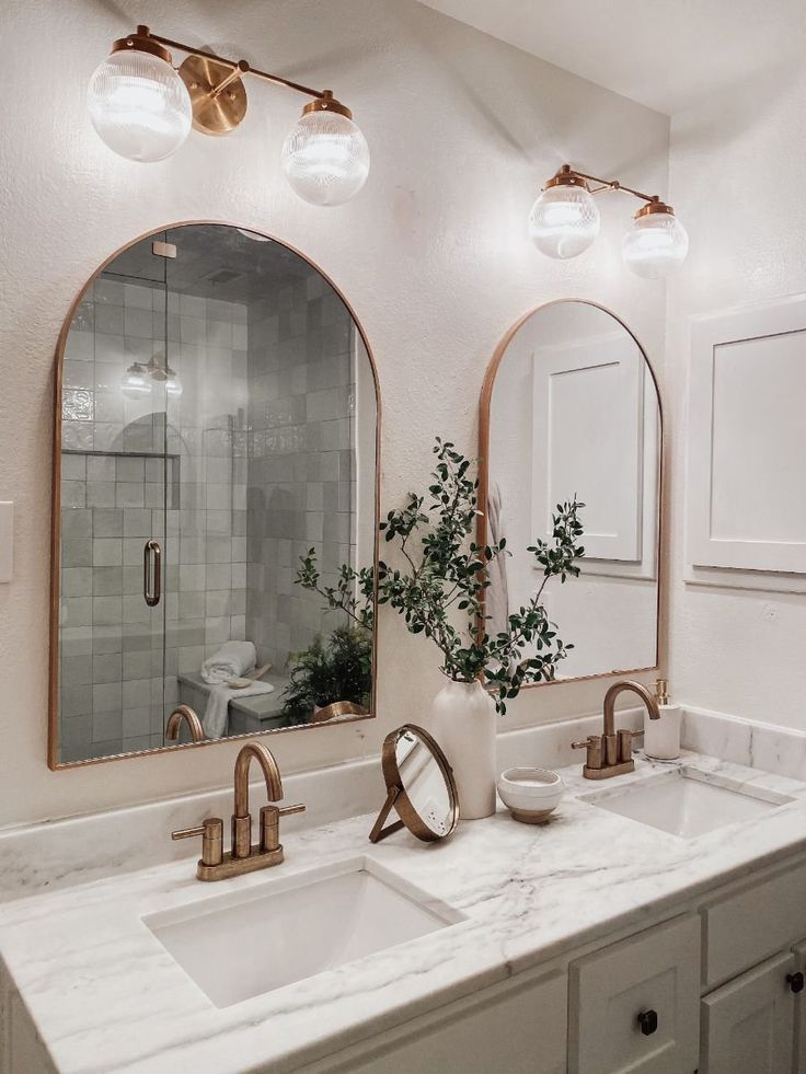 a bathroom with two sinks and three mirrors on the wall, one is white and the other is gold