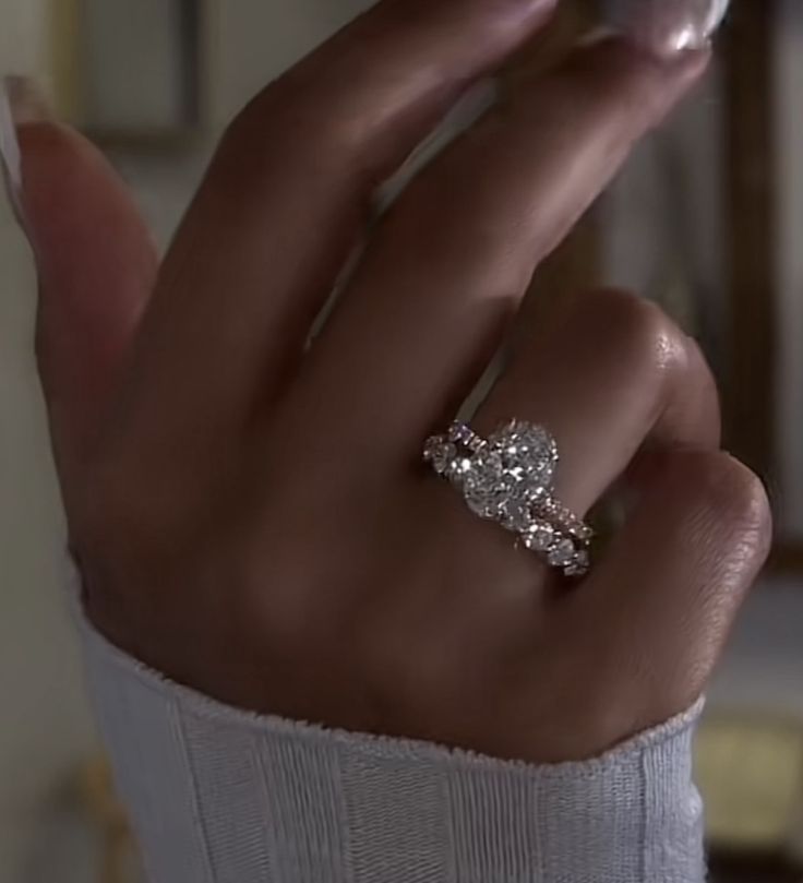 a woman's hand with a diamond ring on her left hand and the other hand holding an object in front of her