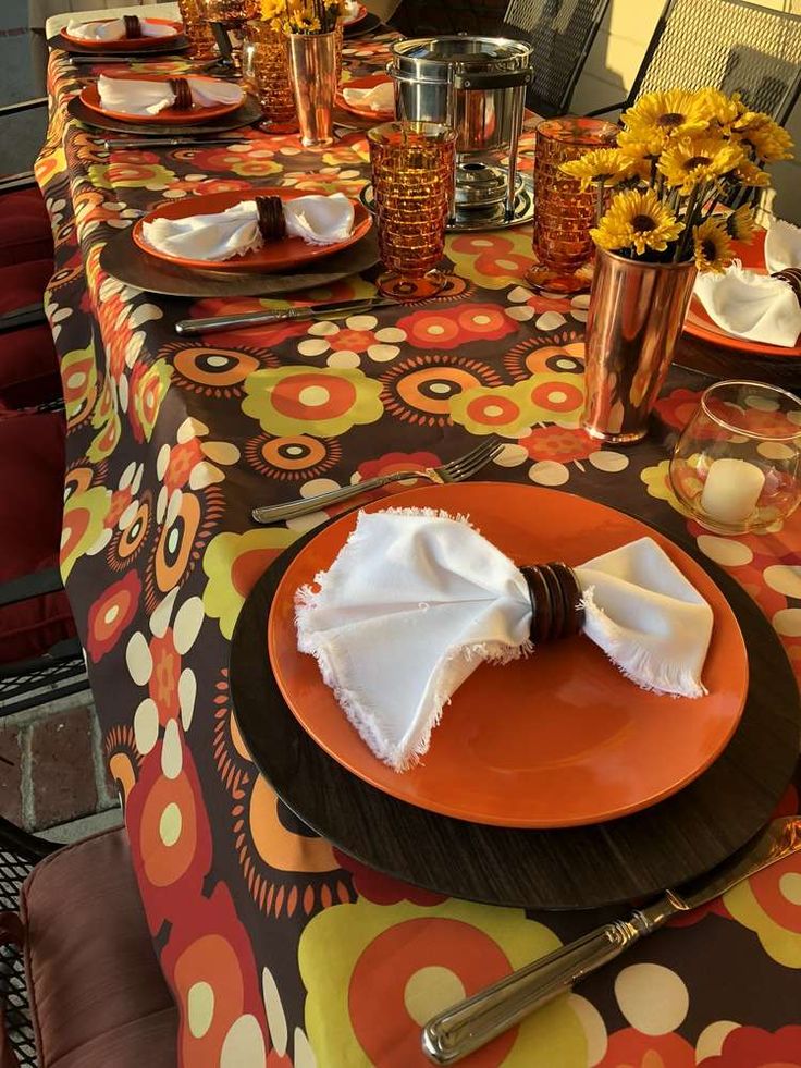 a table set with orange plates and napkins, silverware and flowers in vases