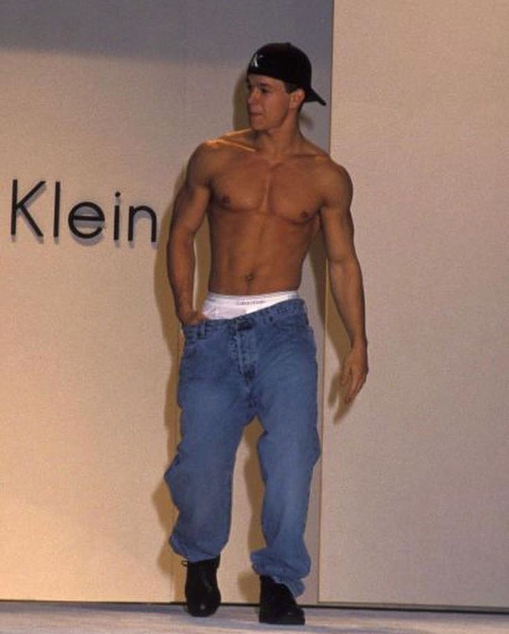 a shirtless man standing in front of a wall with the kleen logo on it