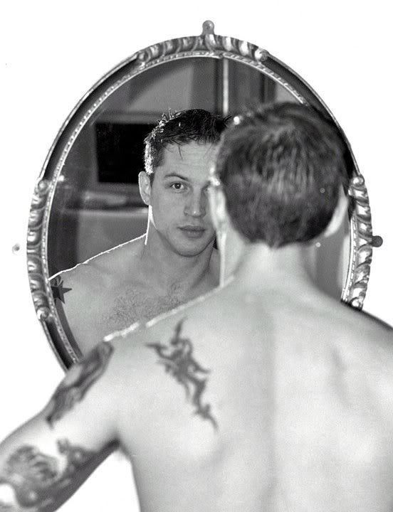 a man looking at himself in the mirror with tattoos on his arm and chest,