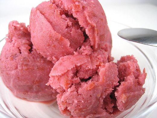 two scoops of pink ice cream on a white plate with a spoon in it