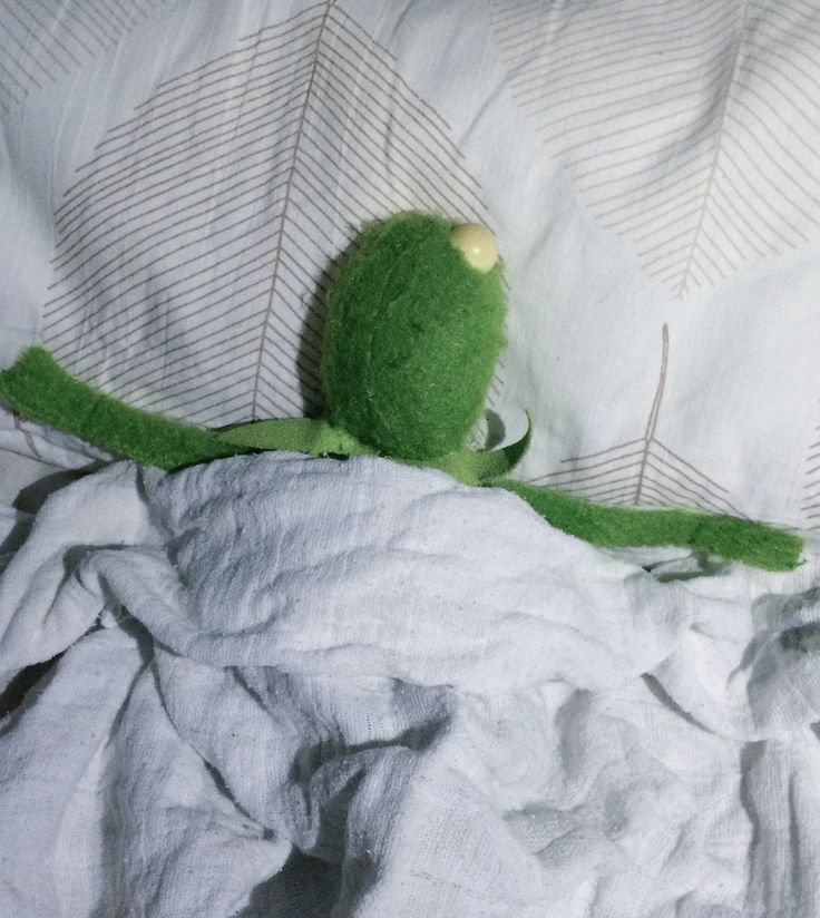 a green stuffed animal sitting on top of a bed