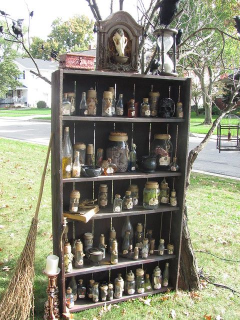 an old wooden shelf with many jars and brooms on it in front of a tree