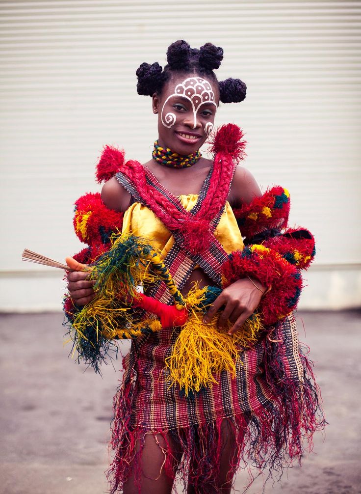 a woman with painted face and head dress holding two sticks in her hands while standing next to a garage door