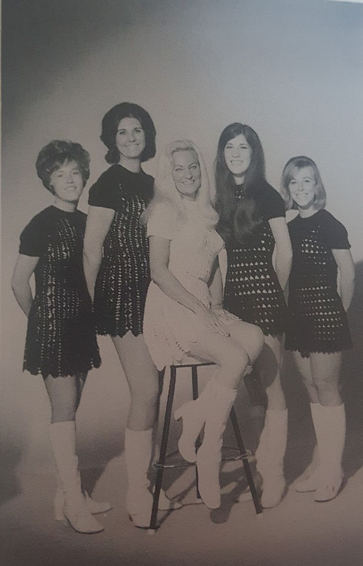 a group of women standing next to each other in short dresses and knee high boots