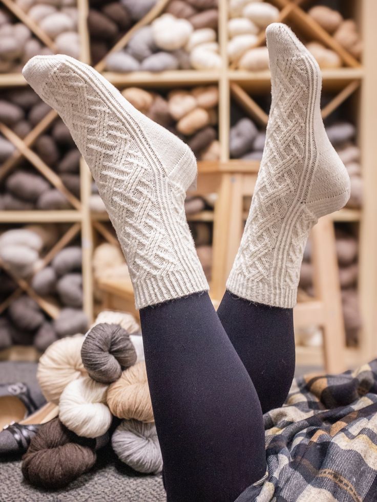 a woman's legs with socks and balls of yarn in the background