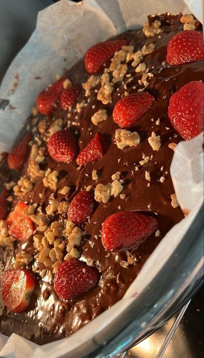 a chocolate cake with strawberries and nuts on top is in a glass dish, ready to be eaten