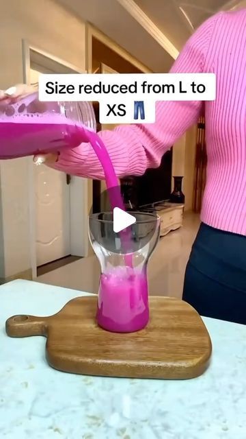 a woman pouring pink liquid into a blender on top of a wooden cutting board