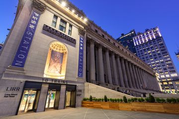 the entrance to an art museum with tall buildings in the background at night, lit up by street lights