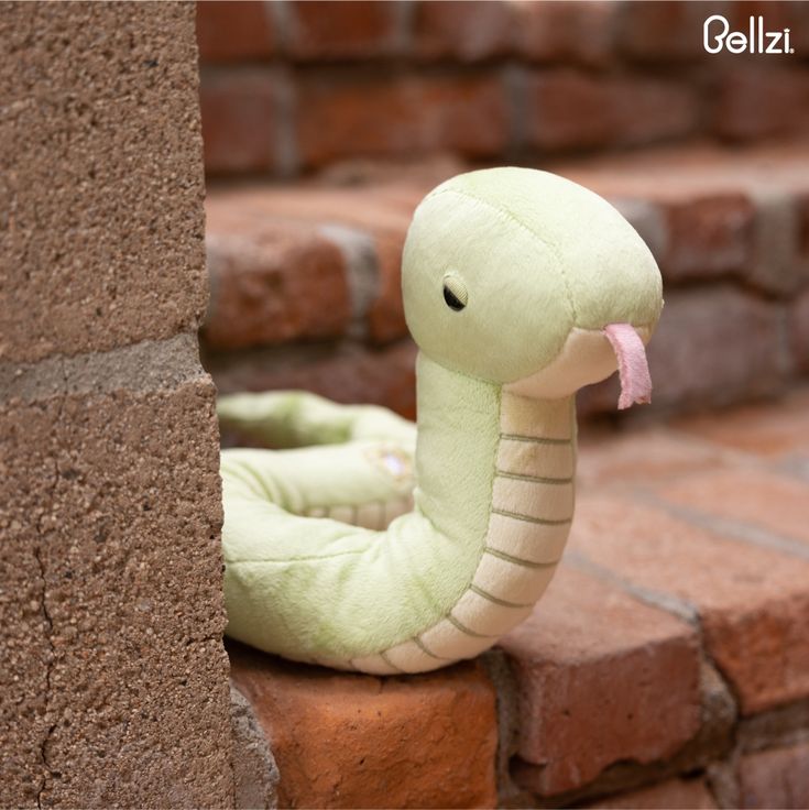 a stuffed snake is sticking its tongue out from behind a brick wall and sitting on the ground