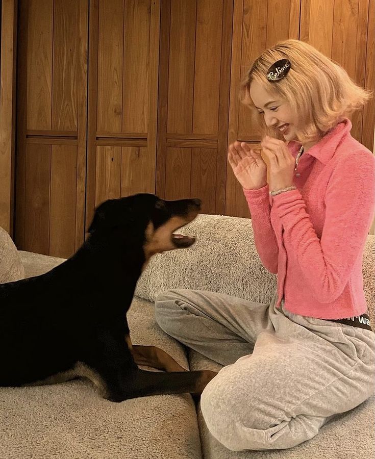 a woman sitting on the couch with her dog and clapping hands to each other while she is petting it's face