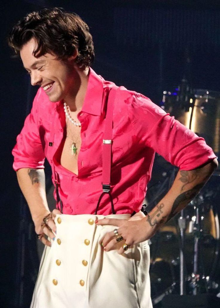 a man in pink shirt and white pants standing on stage with his hands on his hips