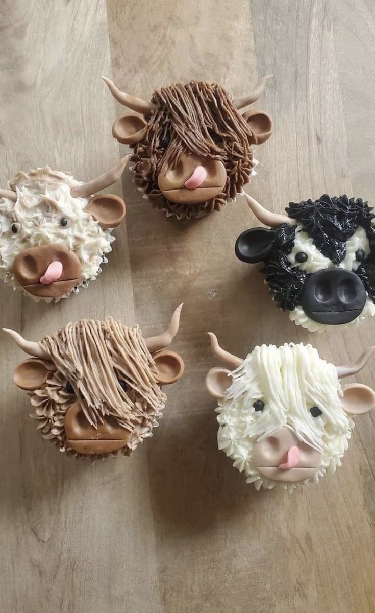 four cupcakes decorated to look like farm animals on a wooden table with white frosting