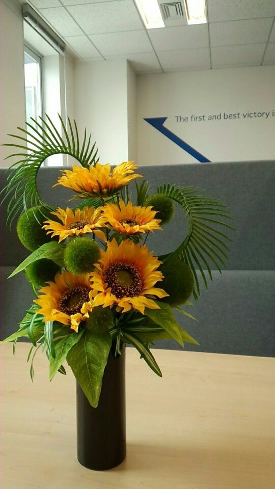 a vase filled with sunflowers on top of a wooden table in an office