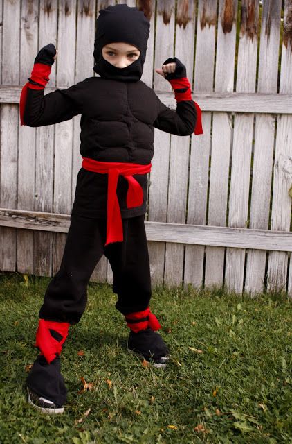 a young boy dressed in ninja gear standing on the grass with his fist raised up