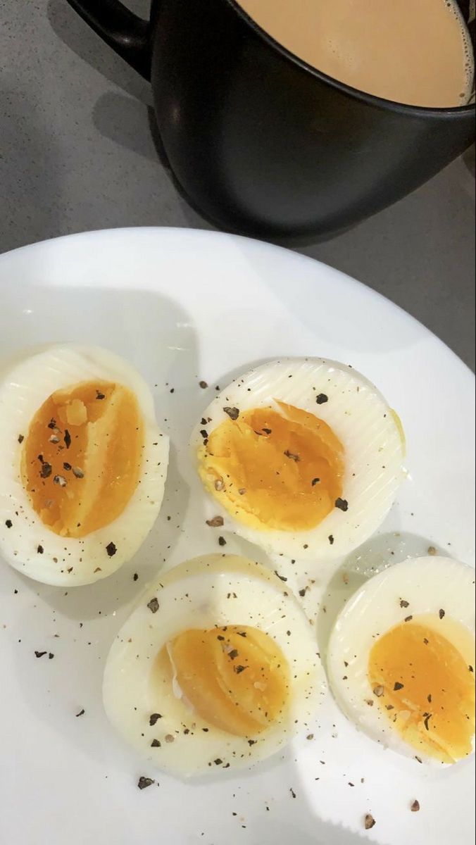 four hard boiled eggs on a white plate next to a cup of coffee and spoon