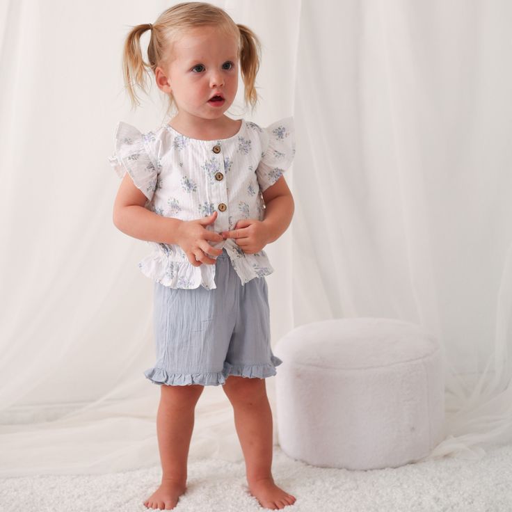 Get ready for some summer fun with the Aliya Skye Short and Top set! These super soft cotton shorts feature an elastic waist for ultimate comfort, while the top boasts flutter sleeves and buttons down the front. Perfect for any little girl, this outfit is sure to become her go-to choice. Wash cold with like colors Lay flat to dry; Minor shrinkage likely if tumble dried 100% cotton Spring Playwear Short-sleeved Tops, Summer Playtime Ruffle Bloomers, Spring Ruffled Shorts For Playwear, Spring Playwear Shorts With Ruffles, Ruffled Bottoms For Summer Playtime, Summer Playwear Tops With Elastic Waistband, Cute Short Tops For Vacation, Cotton Tops With Elastic Waistband For Playwear, Summer Ruffled Short Tops