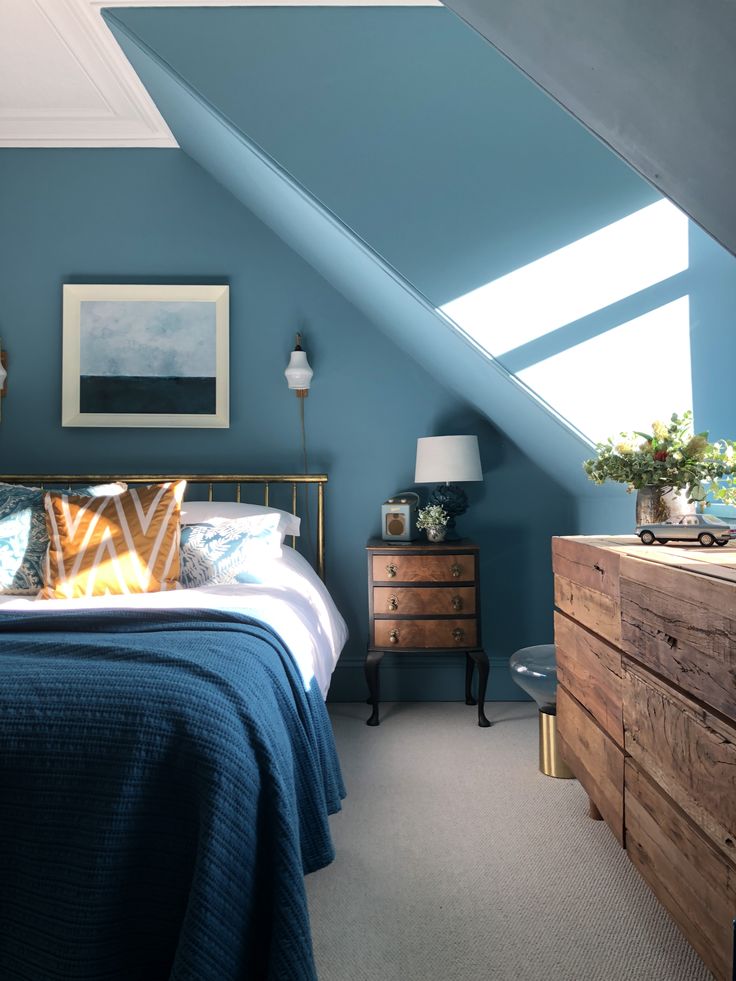 an attic bedroom with blue walls and white bedding, wooden dressers and chest of drawers