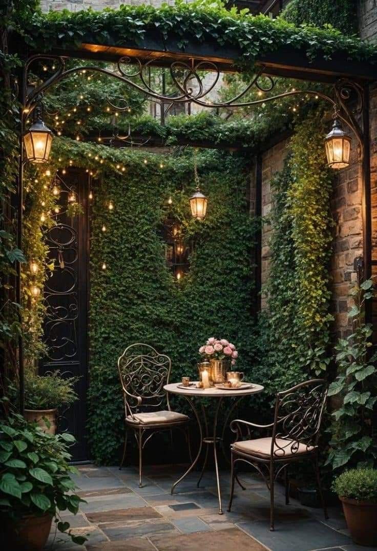 an outdoor dining area with two chairs and a table covered in greenery, surrounded by potted plants