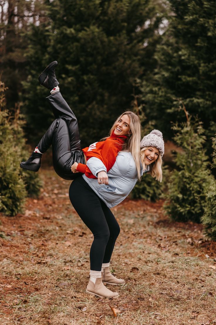 two women are posing for the camera in front of some bushes and trees with one woman upside down on her head