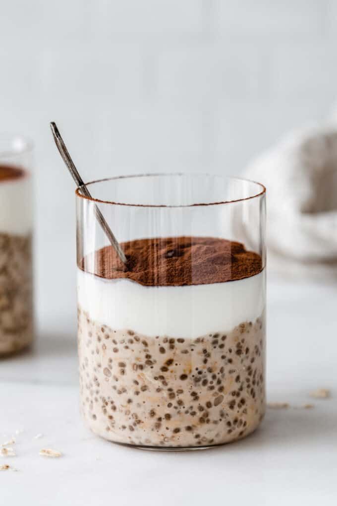 an oatmeal in a glass with a spoon on the side and other food