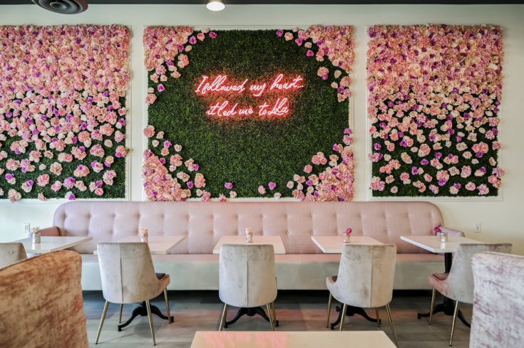 two large floral paintings hang on the wall behind pink velvet banquet tables with white chairs