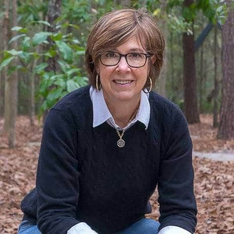 a woman sitting on the ground in front of some trees and leaves with her legs crossed