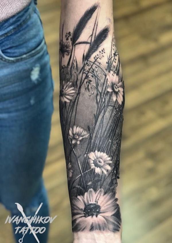 a black and white flower tattoo on the left arm, with daisies in the foreground